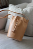 Geöffnete naturfarbene Beuteltasche aus Leder auf einem beigen Sofa
