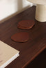 Set aus braunen, asymmetrischen Lederuntersetzern in modernem Wohnzimmer-Ambiente, mit Tasse Cappuccino auf einem Untersetzer