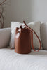 Braune Bucket Bag aus Leder auf einem beigen Sofa im Wohnzimmerambiente