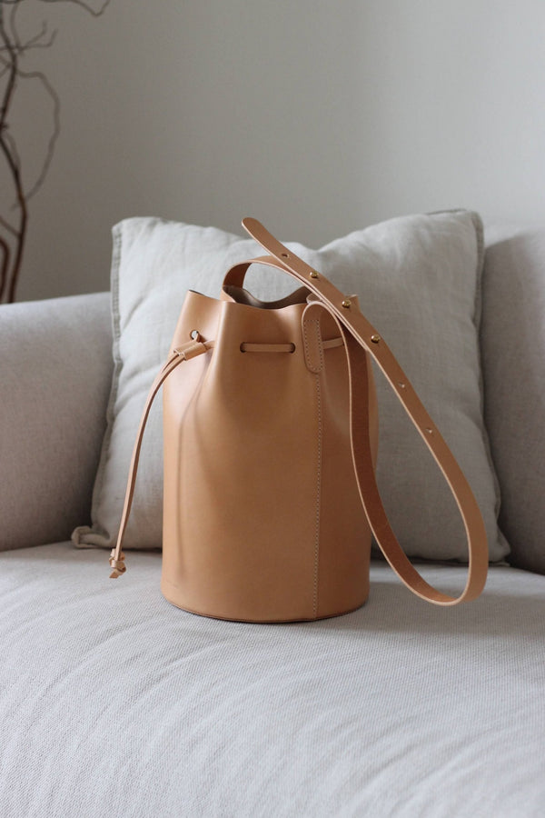 Naturfarbene Bucket Bag aus Leder auf einem beigen Sofa im Wohnzimmerambiente