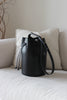 Schwarze Bucket Bag aus Leder auf einem beigen Sofa im Wohnzimmerambiente