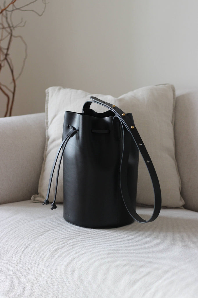 Schwarze Bucket Bag aus Leder auf einem beigen Sofa im Wohnzimmerambiente