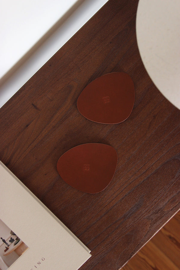 Minimalistische Glasuntersetzer aus braunem Naturleder, organische Form, fotografiert im Wohnzimmer mit Cappuccino