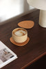 Handgefertigter naturfarbener Getränkeuntersetzer aus Leder auf edler Holzkonsole, darauf ein Cappuccino im Keramikbecher
