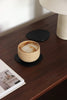 Handgefertigter schwarzer Getränkeuntersetzer aus Leder auf hochwertiger Holzkonsole, dekoriert mit einem Cappuccino